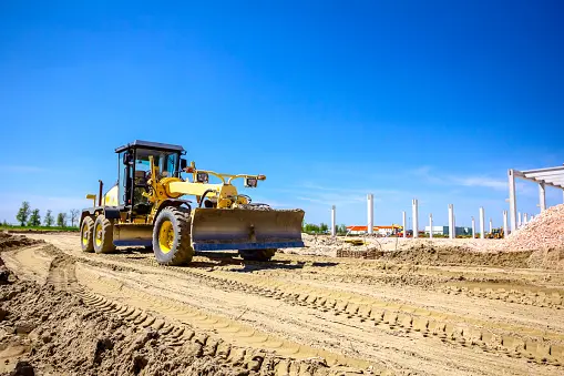 Operator is driving yellow grader, leveling ground at building site. Operator is driving yellow grader, leveling ground at building site.